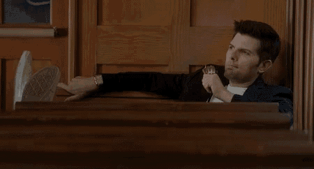 a man in a suit is sitting in a courtroom with his feet up and holding a glass of whiskey .