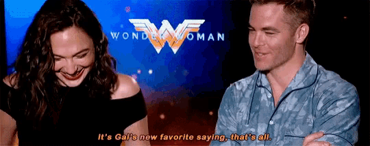 a man and a woman are sitting next to each other and laughing in front of a wonder woman logo .