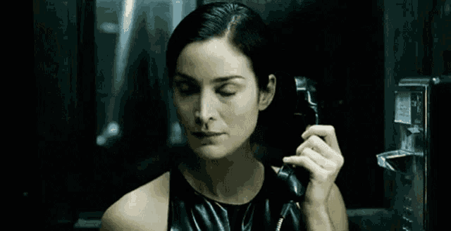 a woman in a black dress is talking on a pay phone .