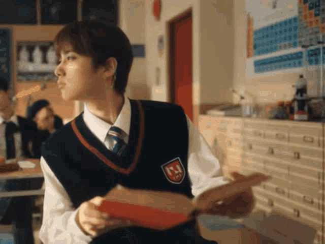a boy in a school uniform is holding a book in a classroom .