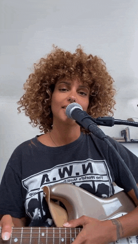 a woman with curly hair is singing into a microphone while holding a guitar
