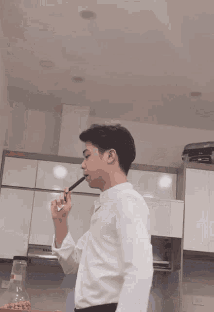 a man in a white shirt is brushing his teeth with a toothbrush