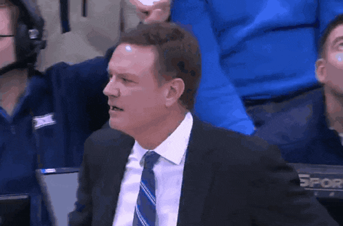 a man in a suit and tie is sitting in the stands watching a game