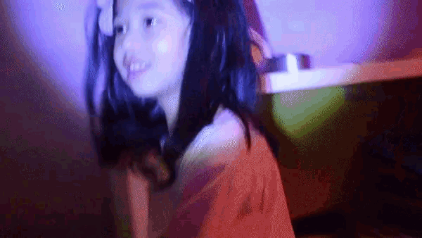 a little girl is sitting in a dark room with a purple light behind her .