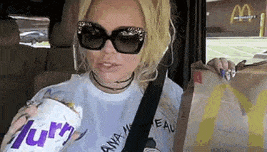 a woman wearing sunglasses is sitting in a car holding a bag of mcdonald 's chicken nuggets .