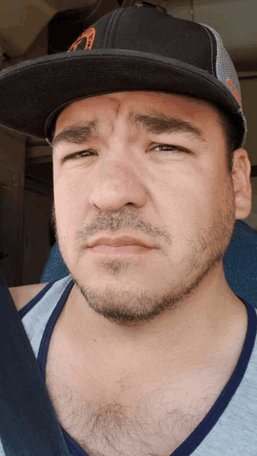 a man with a beard wearing a hat and a grey tank top makes a funny face