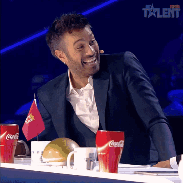 a man in a suit sits at a table with coca-cola cups