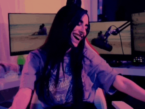 a woman is laughing while sitting in front of a microphone and two monitors .