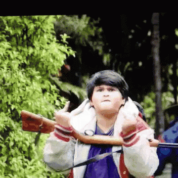 a young boy is holding a rifle and giving a thumbs up sign