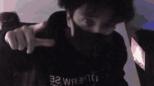 a man wearing a mask is pointing at the camera while standing in front of a computer screen .