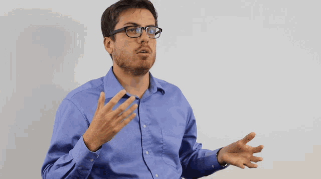 a man wearing glasses and a blue shirt talks with his hands outstretched