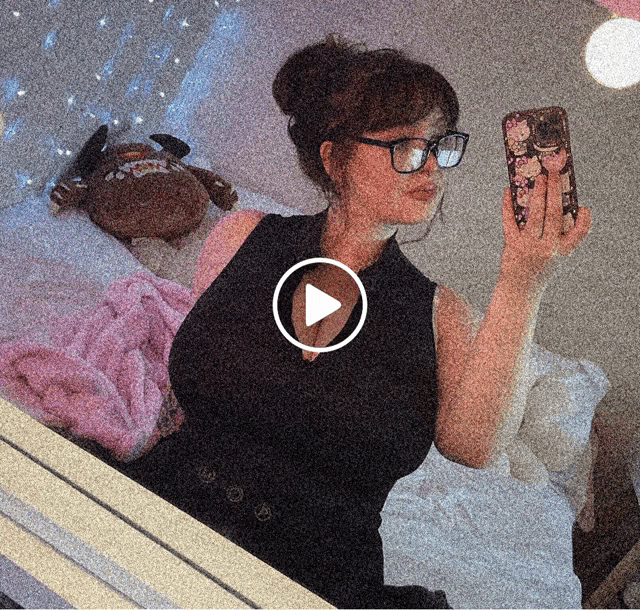 a woman wearing glasses takes a selfie in front of a play button