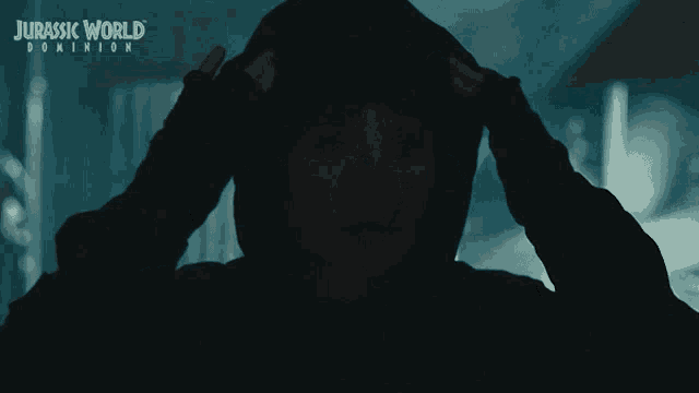 a poster for jurassic world dominion shows a silhouette of a person holding their head