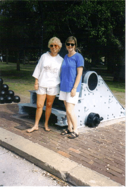 two women are posing for a photo in front of a cannon in a park