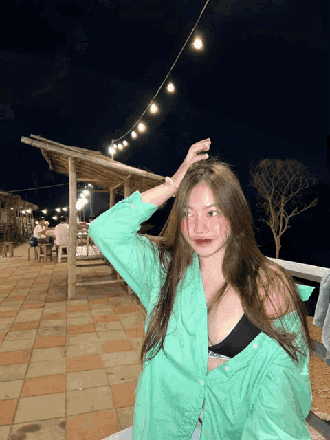 a woman wearing a green shirt and a black bra is standing in front of a string of lights