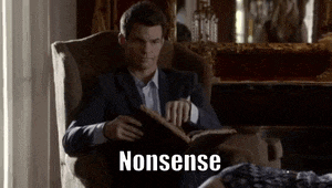 a man in a suit is sitting in a chair reading a book while a woman is laying on the floor .