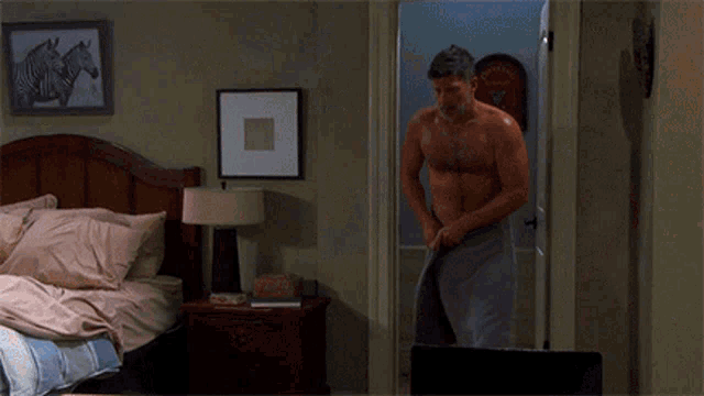a shirtless man wrapped in a towel is standing in front of a bed