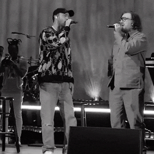 a black and white photo of two men singing into microphones on a stage