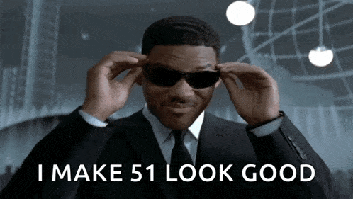 a man in a suit and tie adjusts his sunglasses with the words i make 51 look good behind him