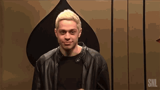 a man in a black leather jacket is standing in front of a ace of spades playing card .