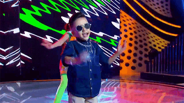 a young boy wearing sunglasses is dancing on a stage