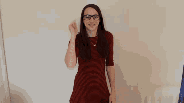 a woman wearing glasses and a red dress is waving