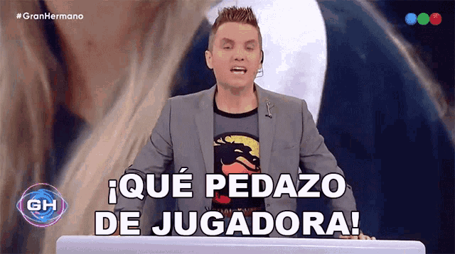 a man in a suit stands at a podium and says que pedazo de jugadora in spanish
