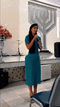 a woman in a blue dress singing into a microphone in front of a menorah