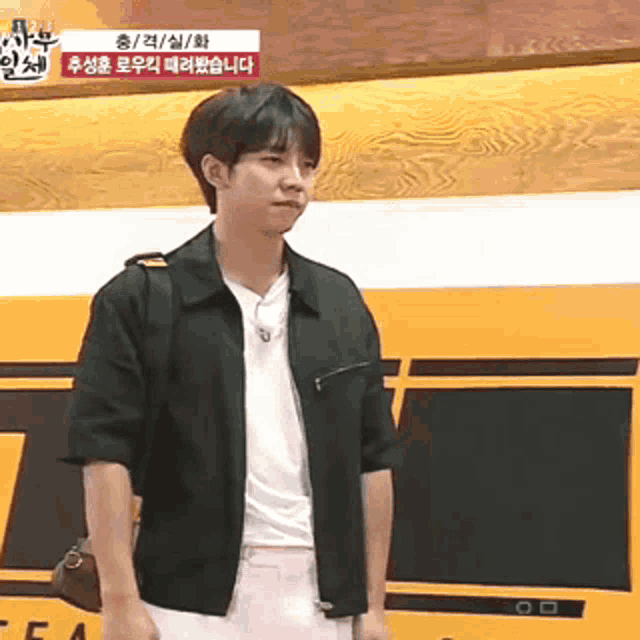 a young man in a black jacket is standing in front of a yellow bus .