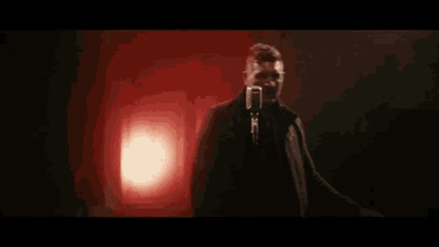a man in a black coat is standing in front of a microphone in a dark room .