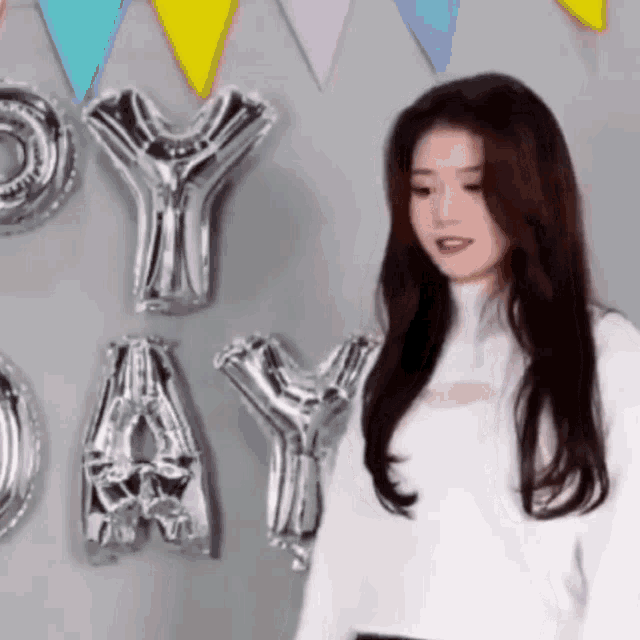 a woman is standing in front of a wall with balloons that spell out happy day .