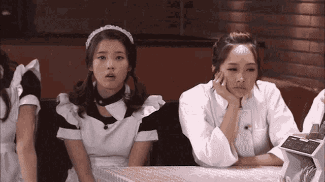 two maids are sitting at a table and one has her hand on her chin