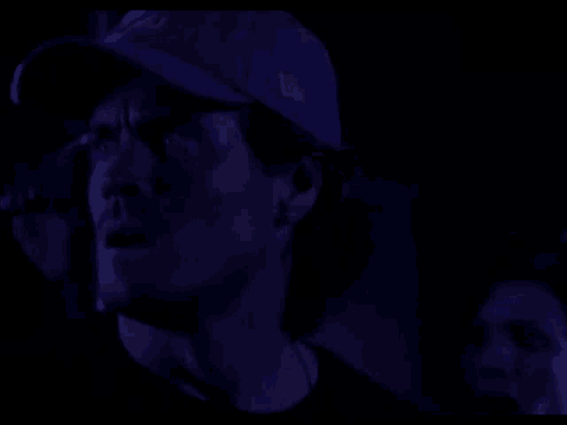 a man wearing a new era hat is looking up in the dark