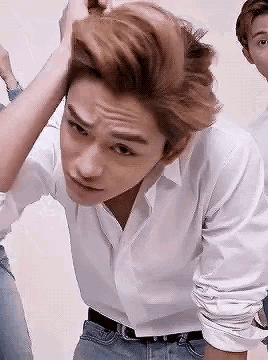 a young man in a white shirt is holding his hair