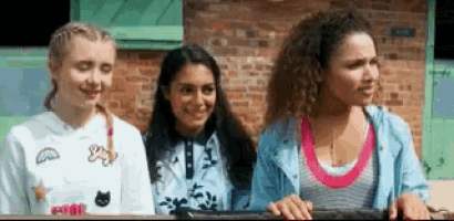 three young women are standing next to each other in front of a brick building .