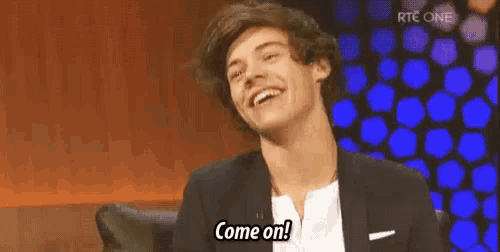 harry styles is smiling and saying `` come on '' while sitting on a chair .
