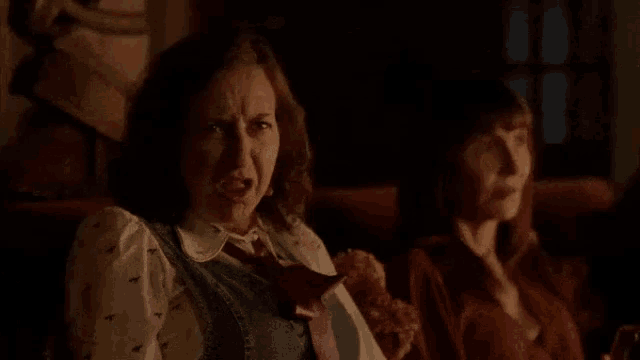 two women are sitting in a dark room watching a movie . one of the women is eating pizza .