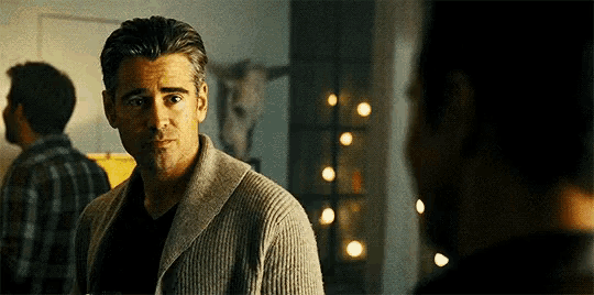 a man in a sweater is looking at another man in a dark room .