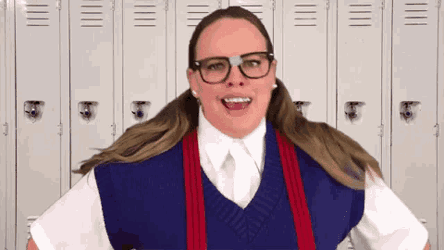 a woman wearing glasses and a sweater vest is standing in front of lockers