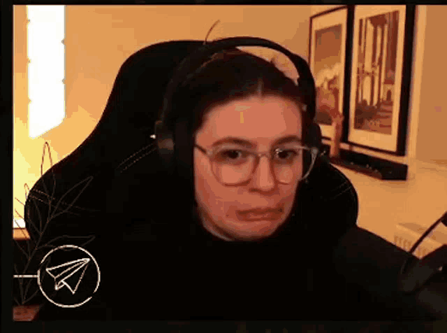 a woman wearing glasses and headphones is sitting in a chair making a funny face .