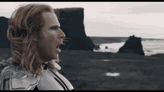 a man with long red hair is standing on a beach with his mouth open