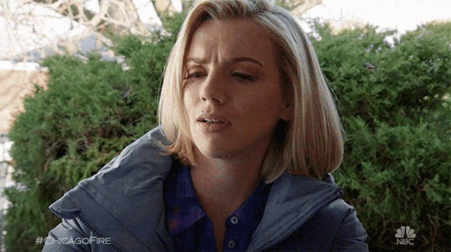 a woman wearing a gray jacket and a blue shirt is making a funny face .