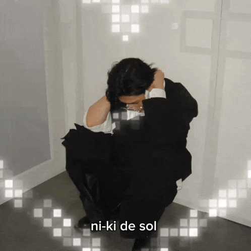 a man in a suit sits in a corner with the words ni-ki de sol written below him