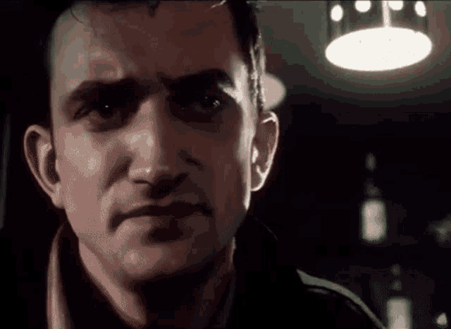 a close up of a man 's face with a light hanging from the ceiling behind him .
