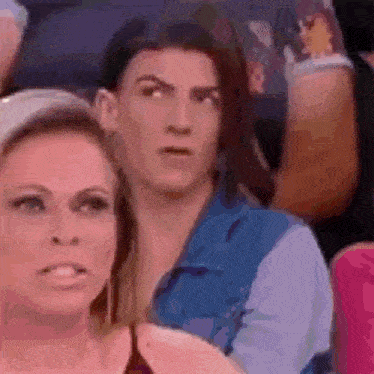 a man and a woman are sitting in a crowd and the woman is making a surprised face .