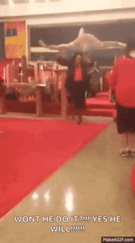 a man in a red shirt is walking down a hallway with the words wont he do it yes he will