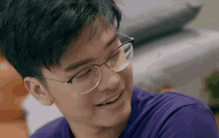 a young man wearing glasses and a purple shirt is smiling and looking down .