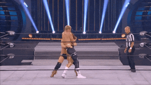 two wrestlers are wrestling in a ring with a referee in the background