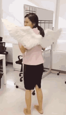 a woman in a pink top and black skirt is holding a large white feathered object