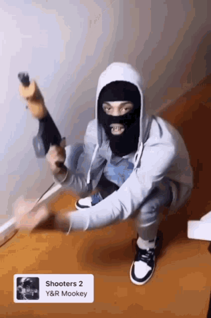 a man wearing a ski mask is kneeling down holding a gun .